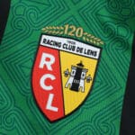 RC Lens 2025/26 away fan jersey badge with club crest, "120" anniversary and green patterned background.