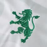 Green lion emblem embroidered on white Sporting CP Away 2025/26 Fan Version jersey fabric.