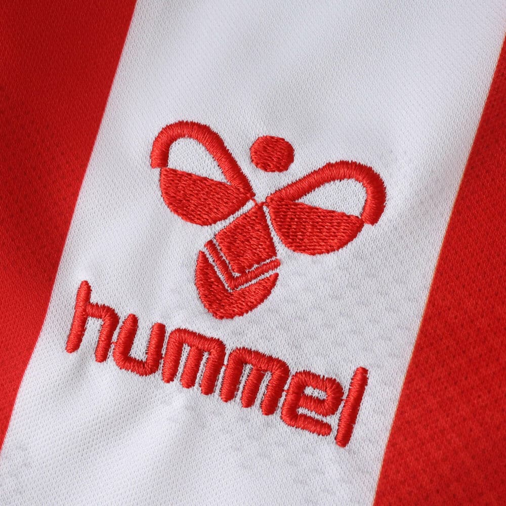 Close-up of the red Hummel logo embroidered on the FC Köln 2025/26 home fan jersey's white stripe.