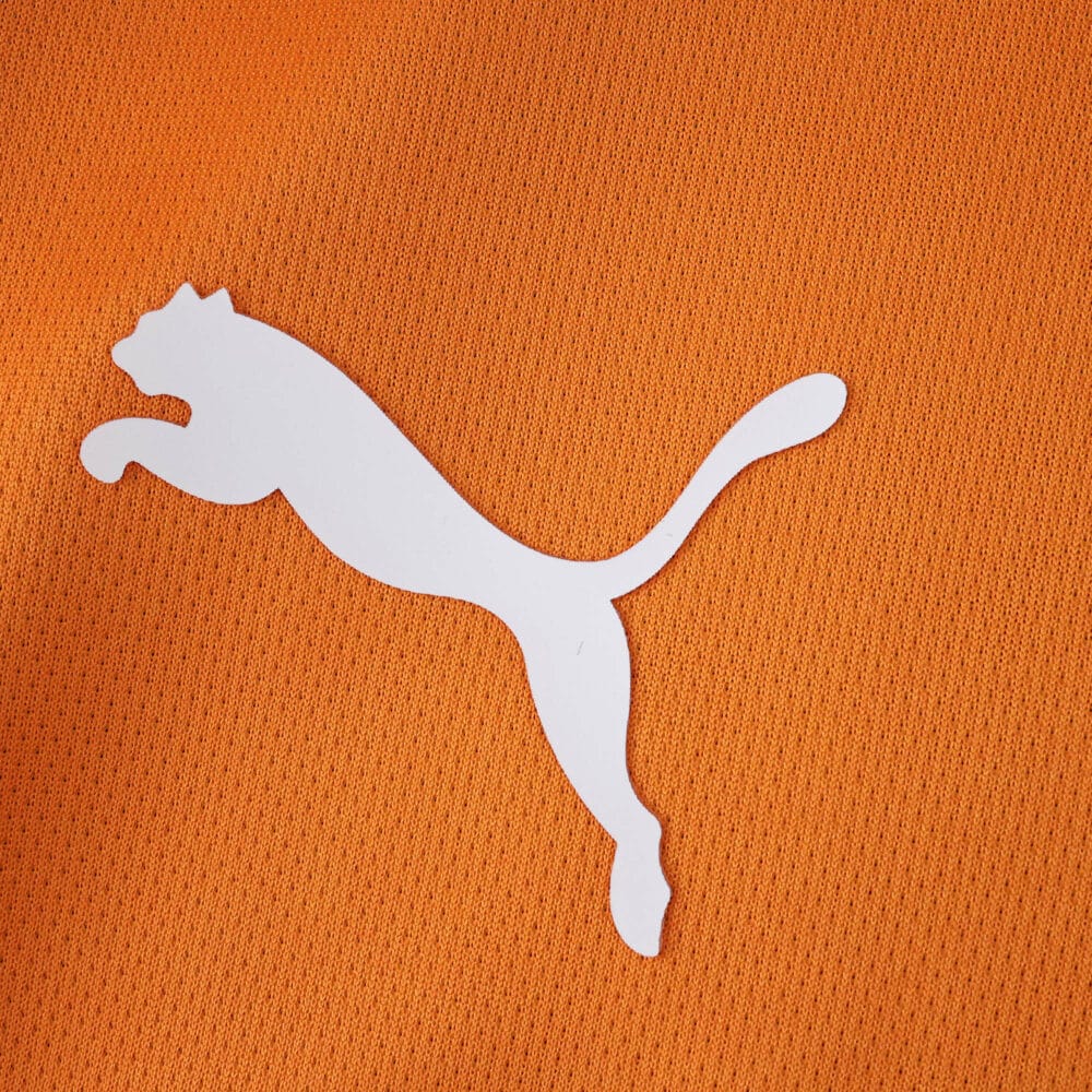Close-up of a white Puma logo on orange fabric, featured on the Galatasaray 2025/26 Home Fan jersey.