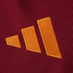Close-up of the Roma 2025/26 fan jersey featuring an orange Adidas logo on red fabric.