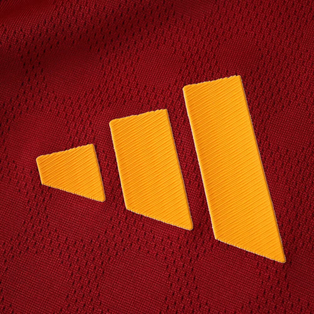 Close-up of the yellow Adidas logo on the red Roma 2025/26 Player Version jersey fabric.