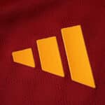 Close-up of the yellow Adidas logo on the red Roma 2025/26 Player Version jersey fabric.