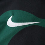 Close-up of Nike logo on the Sporting CP Third 2025/26 Fan Version jersey, green and black fabric visible.