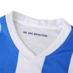 Close-up of the 2025/26 Brighton & Hove Albion home fan jersey, showing blue stripes and "We Are Brighton" inside the collar.