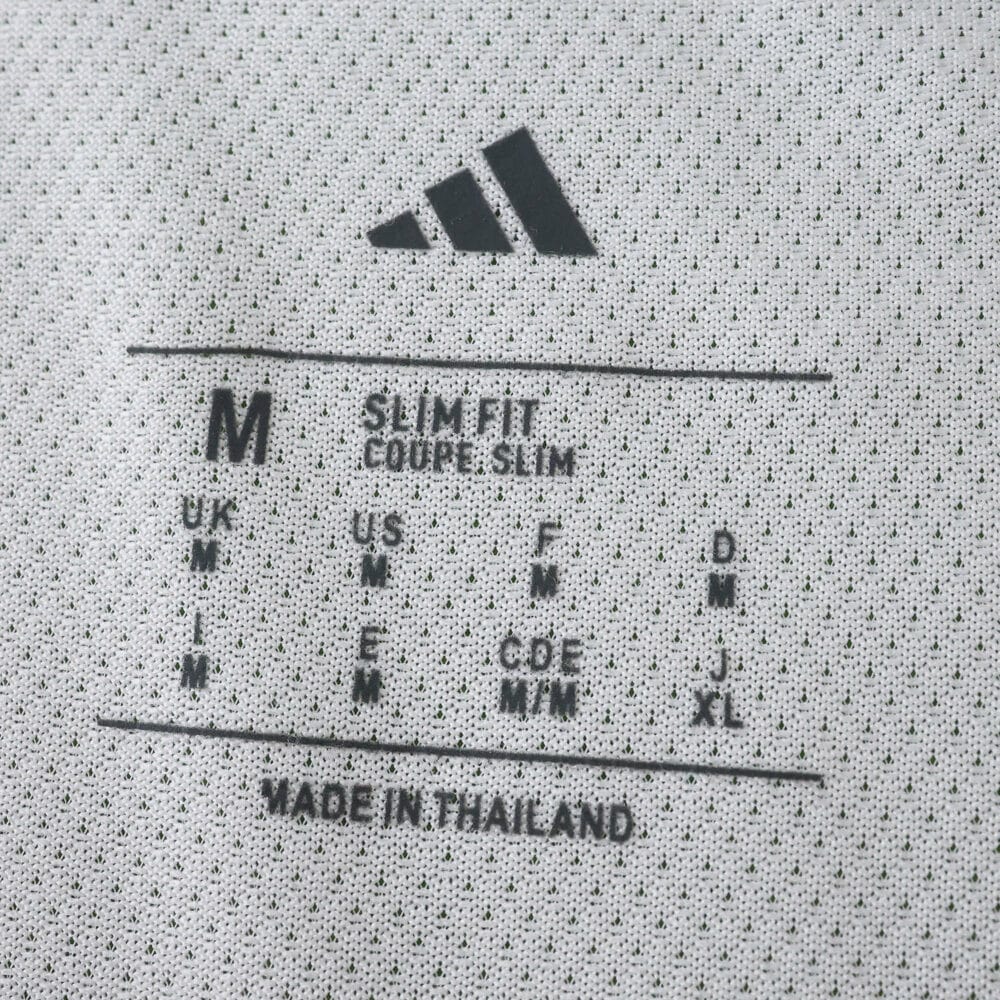 Close-up of the inner tag showing Adidas logo, size M, slim fit info, and 'Made in Thailand' text.