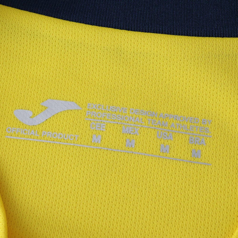 Close-up of Villarreal 2025/26 home fan jersey collar with printed care and size labels in white.