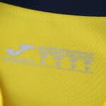 Close-up of Villarreal 2025/26 home fan jersey collar with printed care and size labels in white.