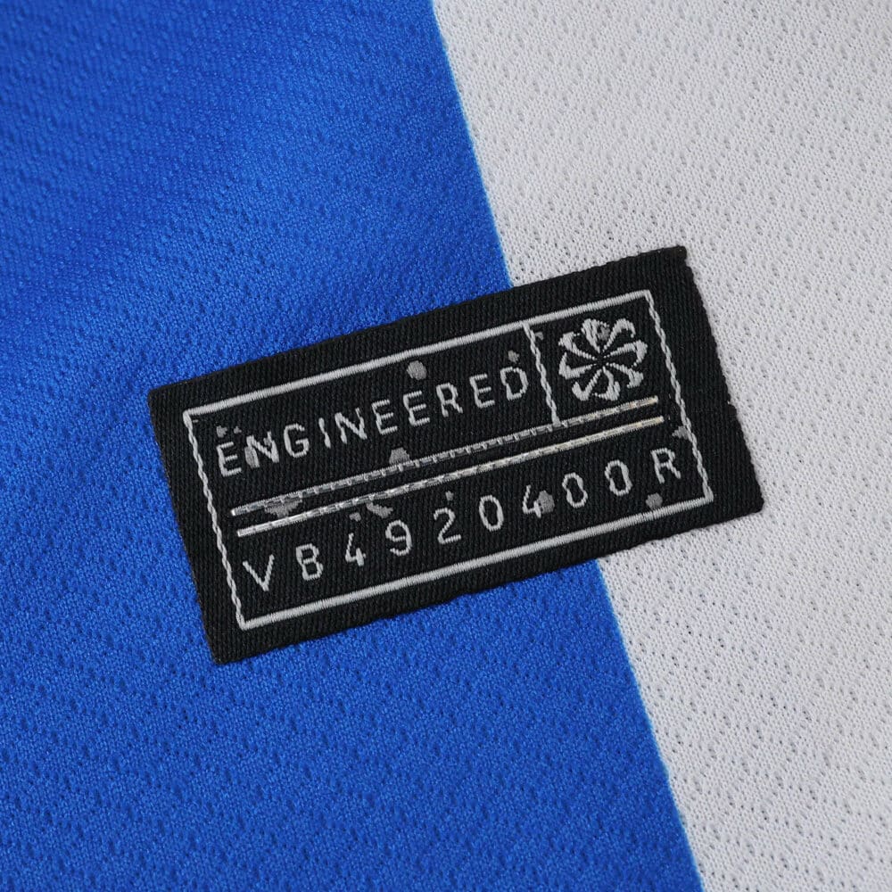 Close-up of the "Engineered" label on the 2025/26 Brighton & Hove Albion Home Fan Version jersey.