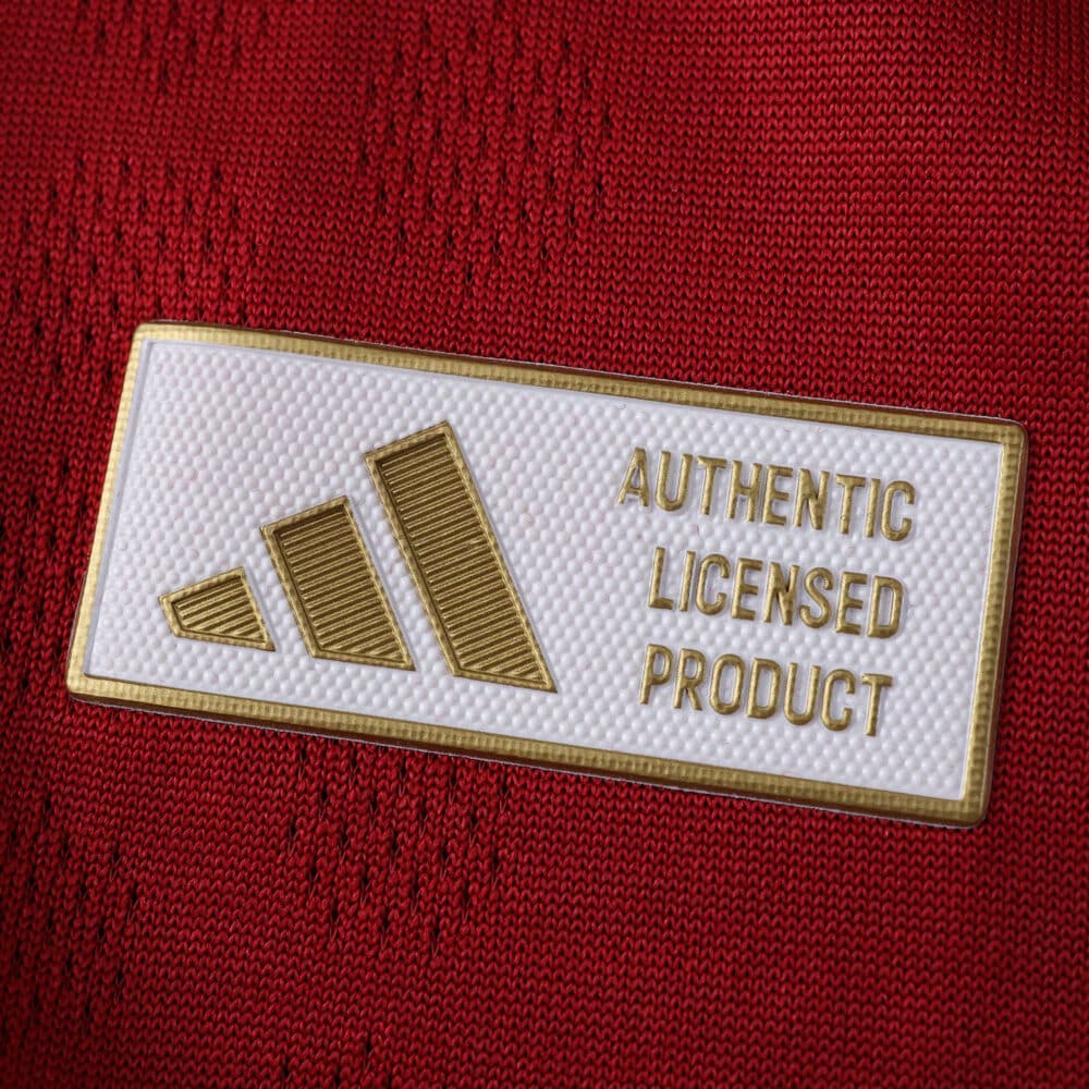 Close-up of the gold Adidas "Authentic Licensed Product" badge on the Roma 2025/26 home player jersey.