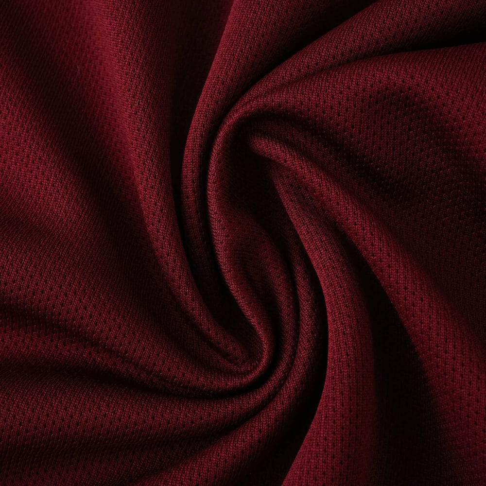 Close-up of West Ham United 2025/26 home fan jersey fabric in deep claret red, showing detailed texture.