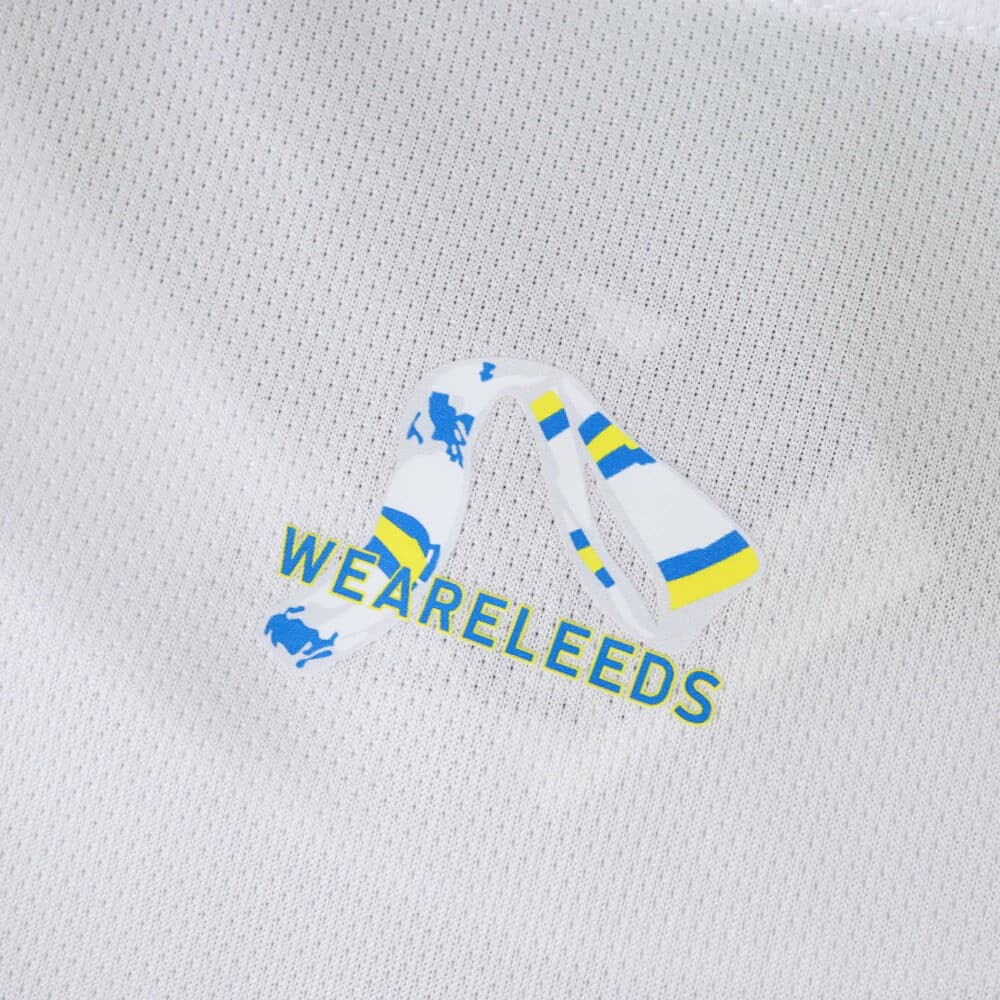 Close-up of Leeds United 2025/26 home fan jersey featuring "WE ARE LEEDS" text and blue-yellow scarf graphic.