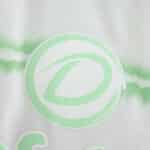 Close-up of the Celtic Third 2025/26 fan jersey featuring a green crest on white fabric with a subtle pattern.