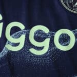Close-up of Ajax 2025/26 Away Player Version jersey featuring partial sponsor logo and textured fabric.