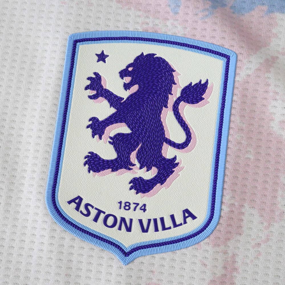 Close-up of the Aston Villa 2025/26 third kit badge featuring a purple lion and "1874" text.