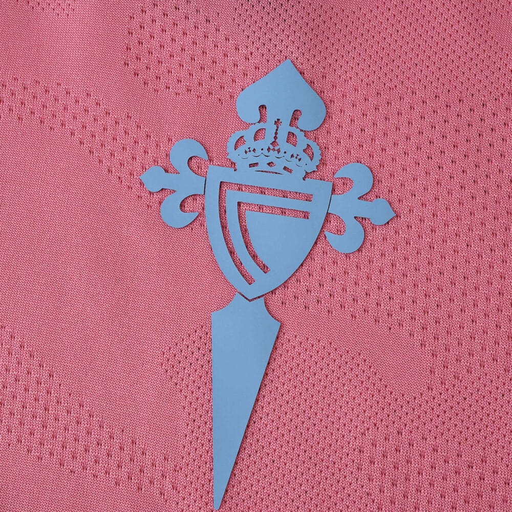 Close-up of the Celta Vigo crest in blue on the pink 2025/26 third fan version football shirt.