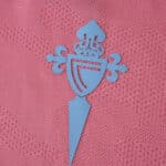 Close-up of the Celta Vigo crest in blue on the pink 2025/26 third fan version football shirt.