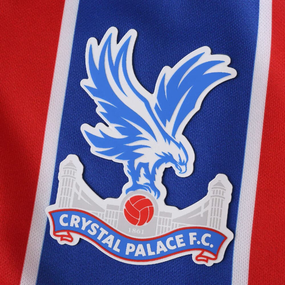 Crystal Palace F.C. crest on the 2025/26 home fan version jersey, featuring a blue eagle over red and blue stripes.
