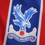 Crystal Palace F.C. crest on the 2025/26 home fan version jersey, featuring a blue eagle over red and blue stripes.