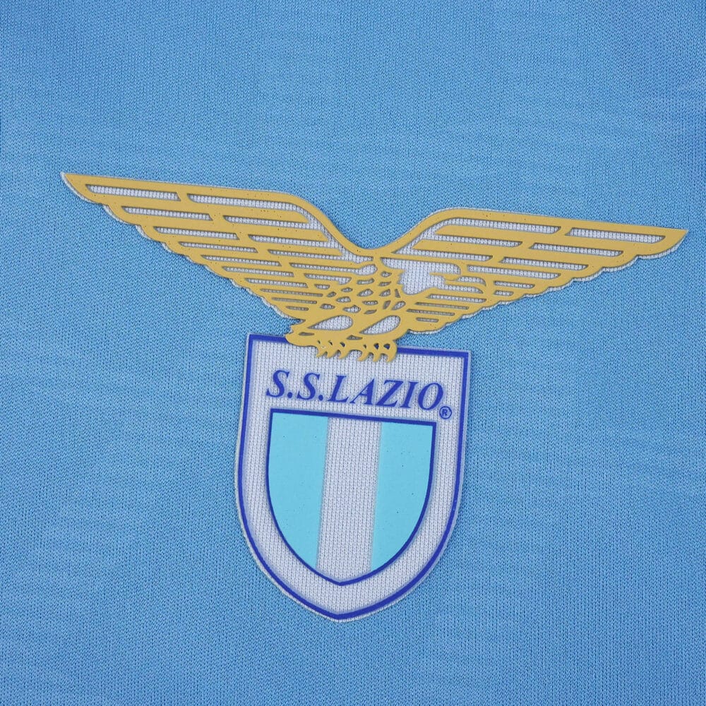 Close-up of the S.S. Lazio club crest on the 2025/26 home fan version jersey fabric.