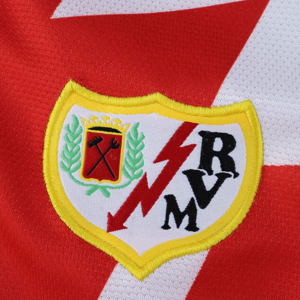 Close-up of the Rayo Vallecano 2025/26 home jersey crest with red lightning bolt and club initials.