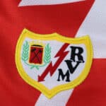 Close-up of the Rayo Vallecano 2025/26 home jersey crest with red lightning bolt and club initials.
