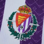 Close-up of the Real Valladolid crest on the 2025/26 home fan version jersey, purple and white background.