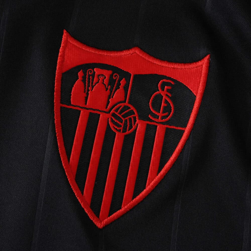 Close-up of the Sevilla FC 2025/26 Third Jersey Fan Version crest in red on black fabric.
