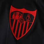 Close-up of the Sevilla FC 2025/26 Third Jersey Fan Version crest in red on black fabric.