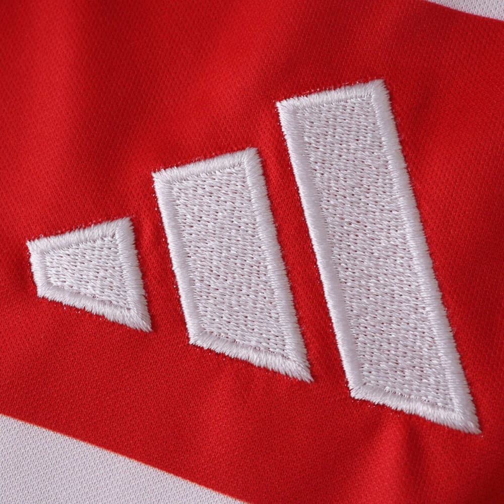 Close-up of the white Adidas logo stitched on the red and white Granada Home 2025/26 Fan Version jersey fabric.