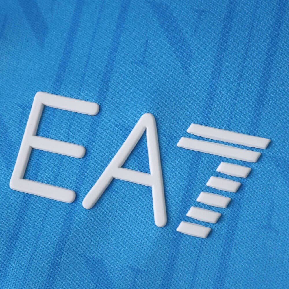 Close-up of the white EA7 logo on the blue Napoli Home 2025/26 Fan Version jersey fabric.