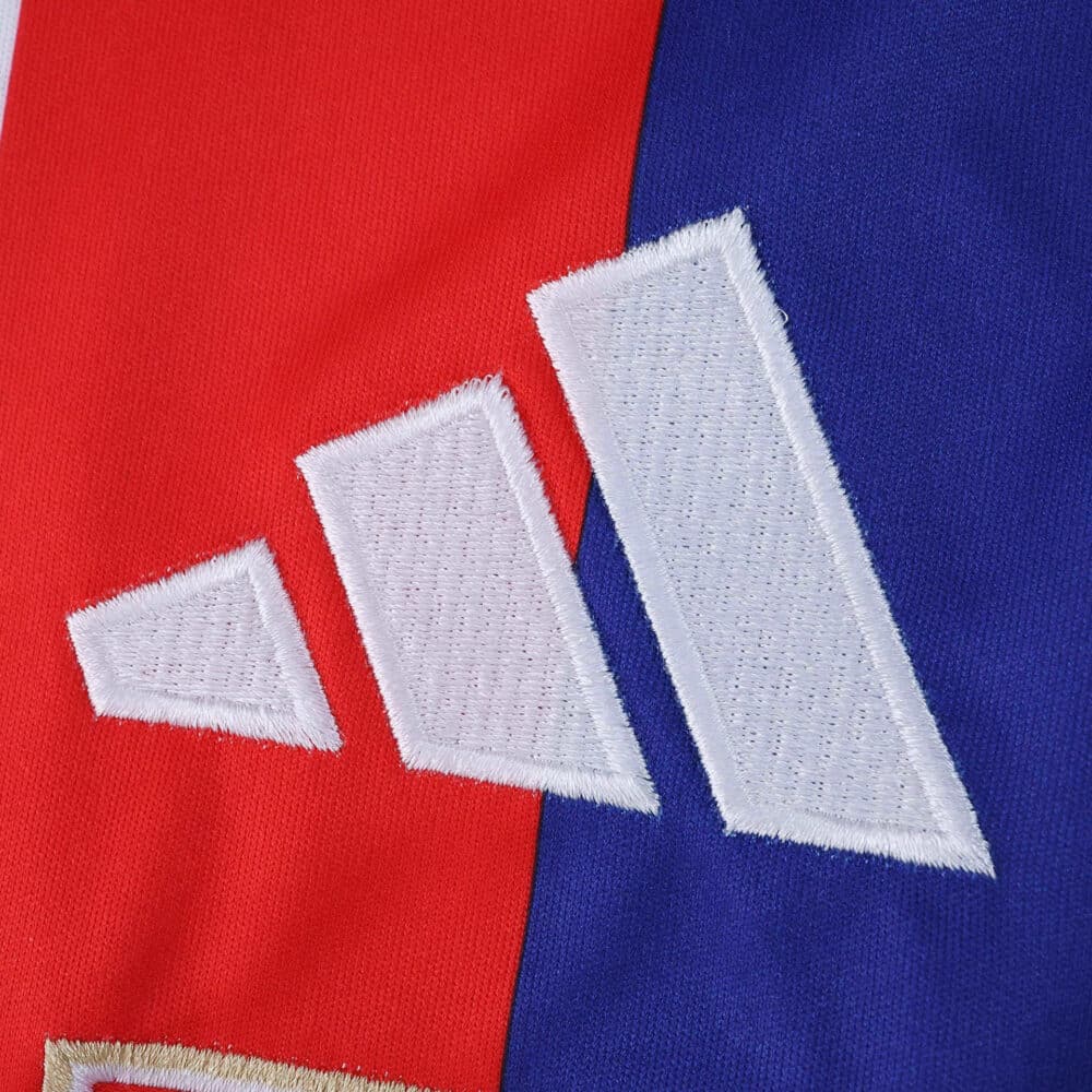 Close-up of Adidas logo on Olympique Lyonnais 2025/26 home fan jersey, red and blue background.