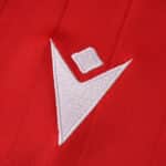Close-up of the Macron logo embroidered on the red Osasuna Home 2025/26 Fan Version jersey.