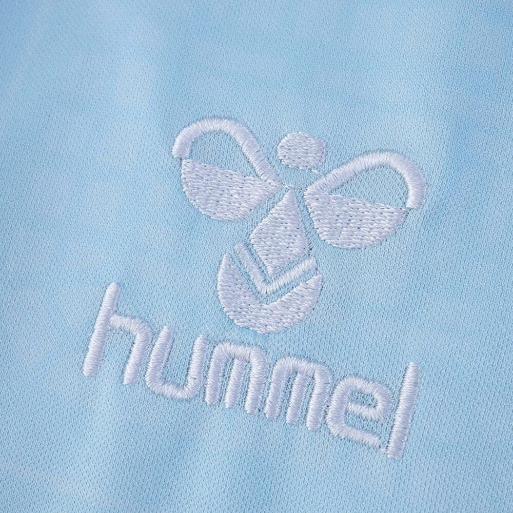 Close-up of white Hummel logo embroidered on the light blue Real Betis 2025/26 away fan jersey fabric.