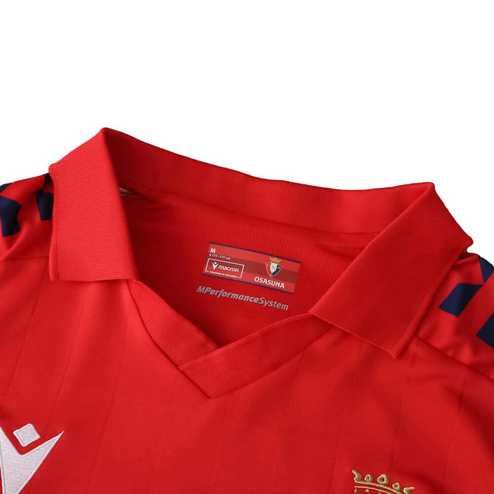 Close-up of the Osasuna 2025/26 home fan jersey collar with red fabric and embroidered club crest.