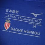 Close-up of AS Monaco Away 2025/26 Fan Version jersey tag with club crest, Mizuno logo, and sizing details.