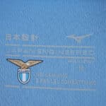 Close-up of Lazio 2025/26 home fan jersey tag with club crest and "Noi l'amiamo e per lei combattiamo" text.