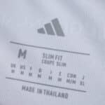 Close-up of Olympique Lyonnais 2025/26 Home Fan Version shirt size tag, showing slim fit and made in Thailand.