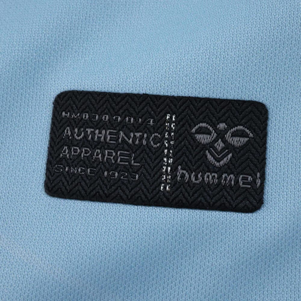 Close-up of Hummel Authentic Apparel patch on the 2025/26 Real Betis away fan jersey in light blue fabric.