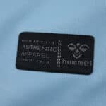 Close-up of Hummel Authentic Apparel patch on the 2025/26 Real Betis away fan jersey in light blue fabric.