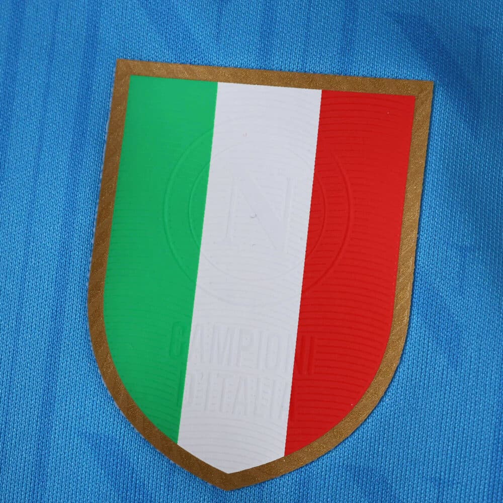 Close-up of the Napoli 2025/26 home fan jersey featuring a badge with Italy's tricolor shield.