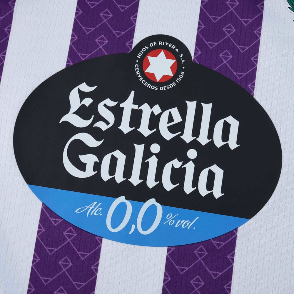 Close-up of the Estrella Galicia 0.0% sponsor logo on the Real Valladolid 2025/26 home fan jersey.