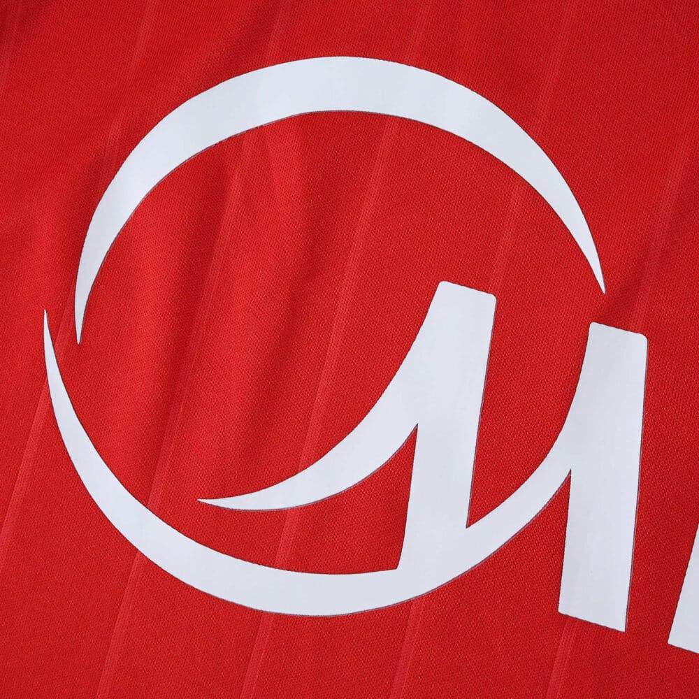 Close-up of the Sevilla FC Away 2025/26 Fan Version jersey showing part of the white sponsor logo on red fabric.