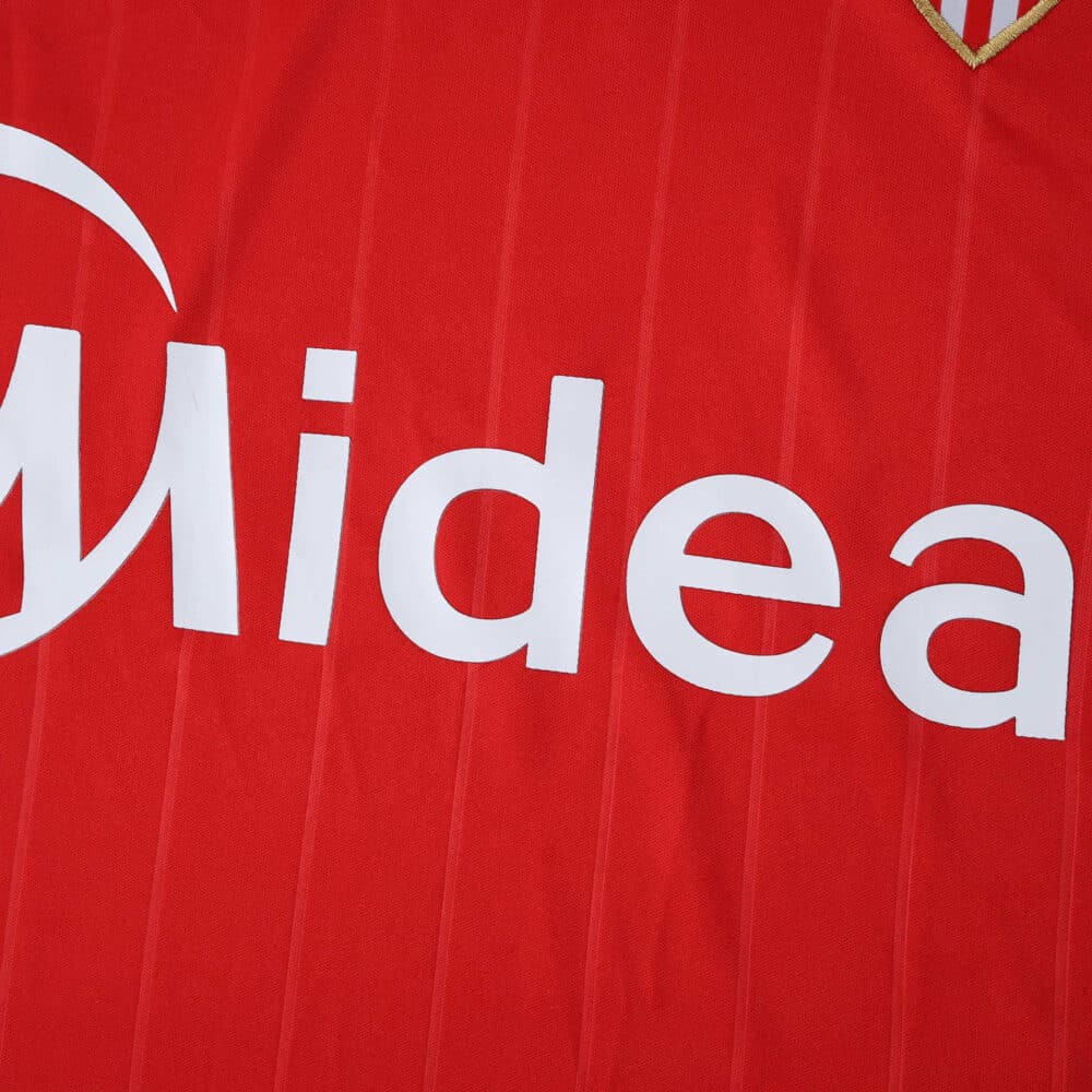 Close-up of Sevilla FC Away 2025/26 Fan Version jersey showing sponsor logo on red fabric.
