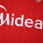Close-up of Sevilla FC Away 2025/26 Fan Version jersey showing sponsor logo on red fabric.