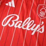 Close-up of Nottingham Forest 2025/26 home fan jersey showing club crest, sponsor, and adidas logo on red fabric.